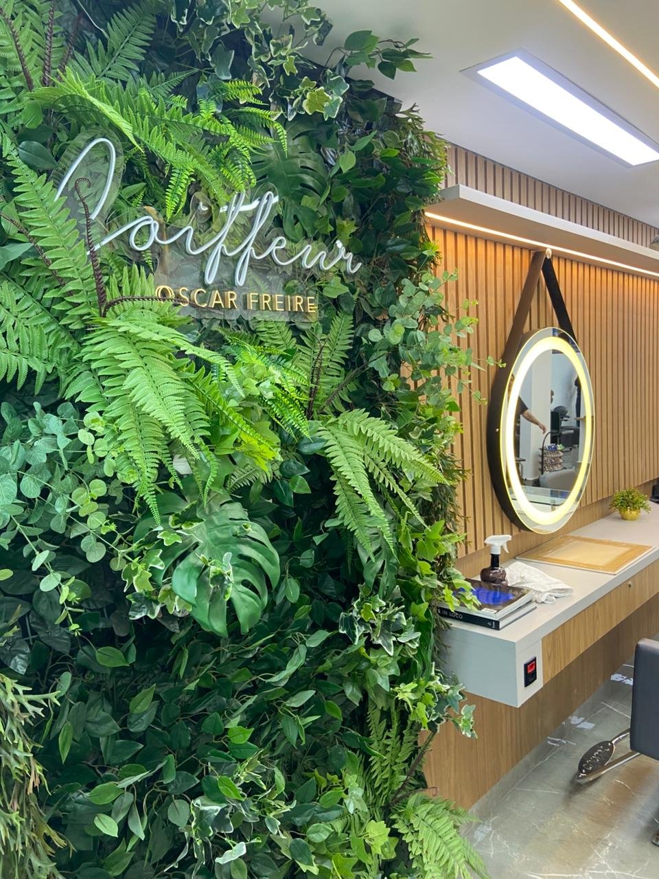 Jardim vertical do salão com o letreiro neon Coiffeur Oscar Freire e espelho iluminado