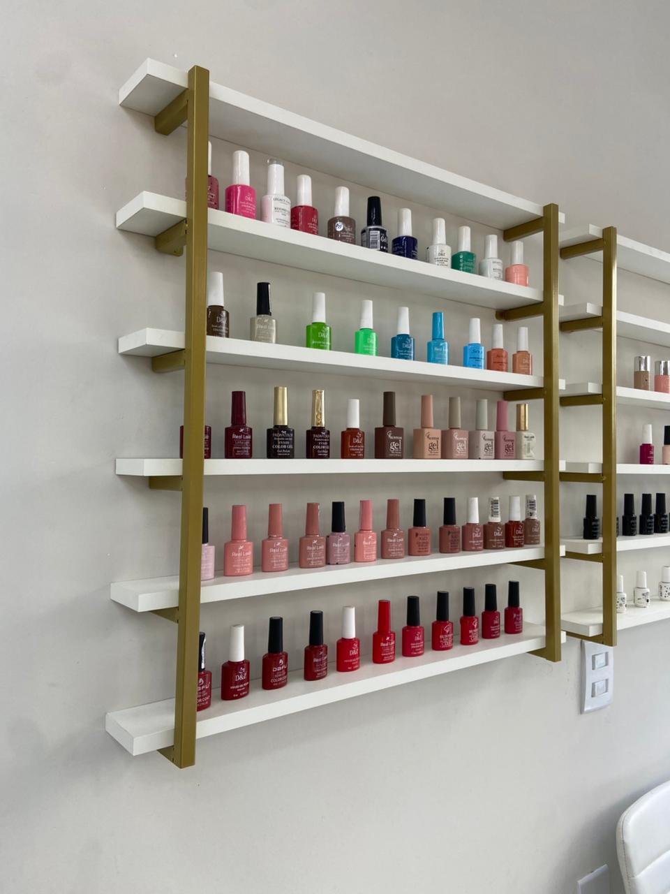 Parede com prateleiras douradas repletas de esmaltes coloridos para manicure
