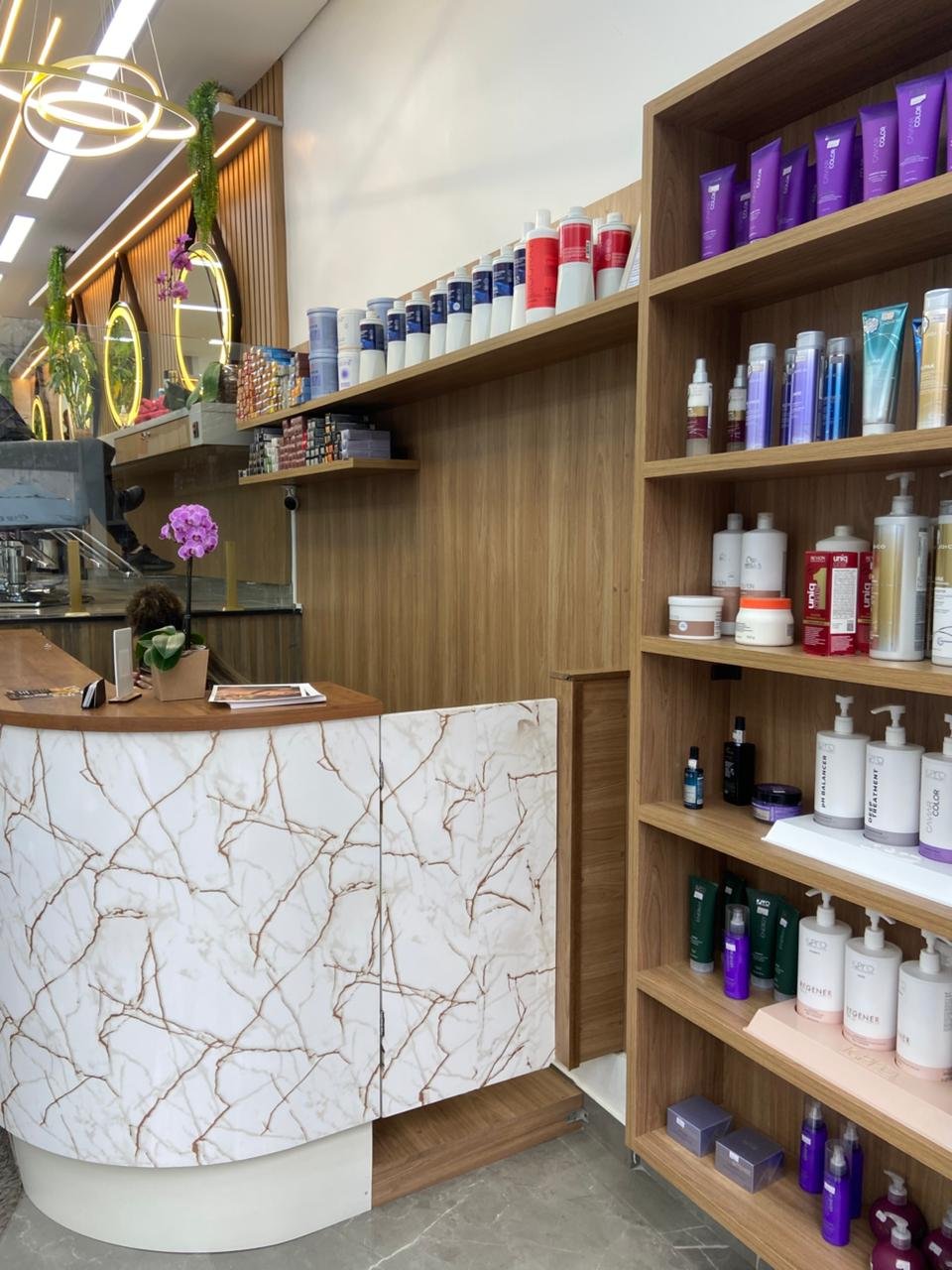 Recepção com balcão de mármore branco e estante de produtos profissionais de cabelo